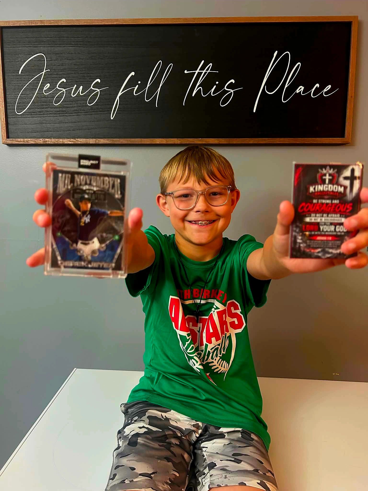 Smiling boy holding collectible cards under a sign saying "Jesus fill this Place".