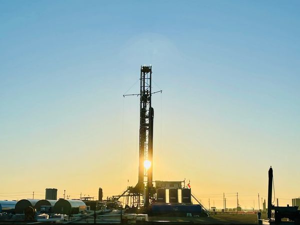 Oil drilling rig silhouetted against a sunrise with clear sky.