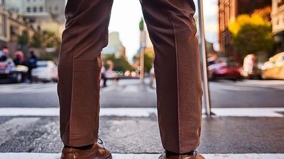 Close up view of the back of a man's lower legs as he crosses a busy street.
