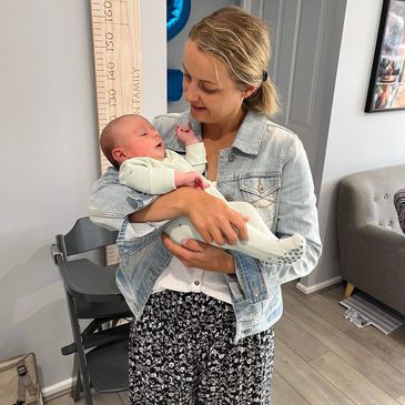 A blonde woman in a denim jacket affectionately holding a small baby.