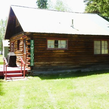 Rustic wooden cabin named Sawtooth in a grassy area.