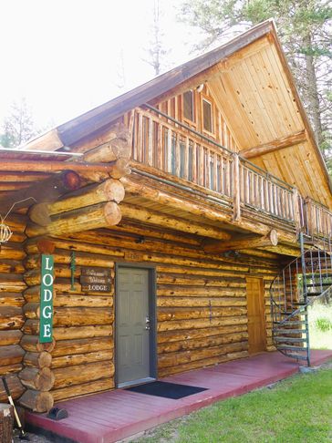 Rustic wooden lodge with balcony and spiral staircase.