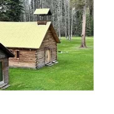 Wooden cabin on green lawn with trees.