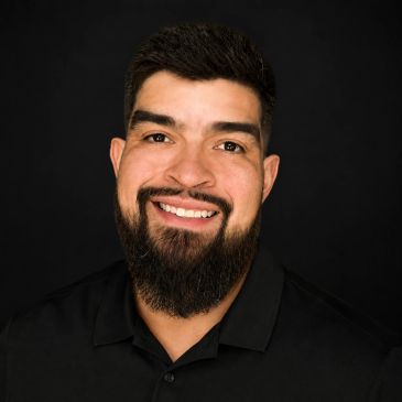 Smiling man with beard in black shirt against a dark background.