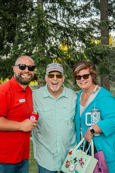 Three smiling people outdoors wearing sunglasses.