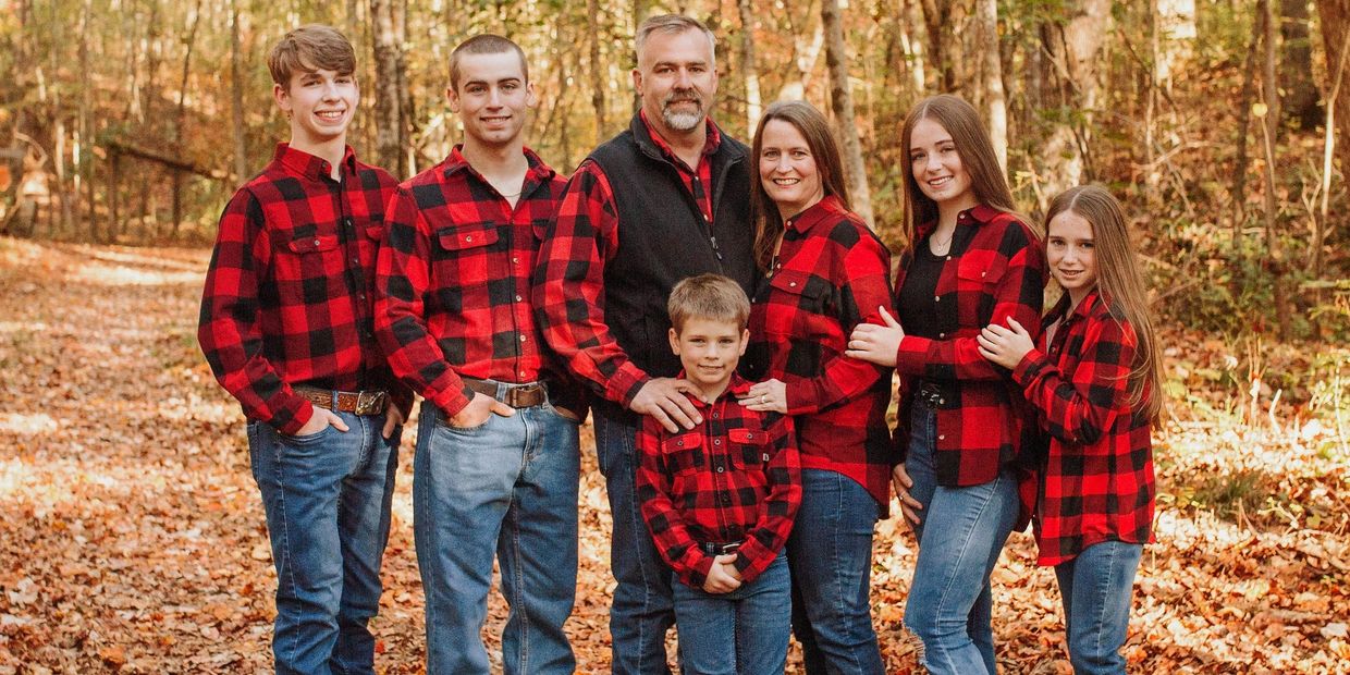 Family in matching red plaid shirts in autumn forest.