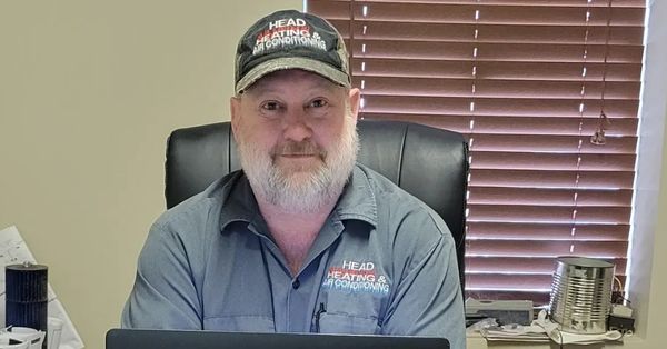 Man in work uniform sitting at a desk with blinds behind.