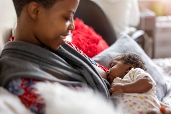 A woman is sitting on the couch with pillows breastfeeding her baby