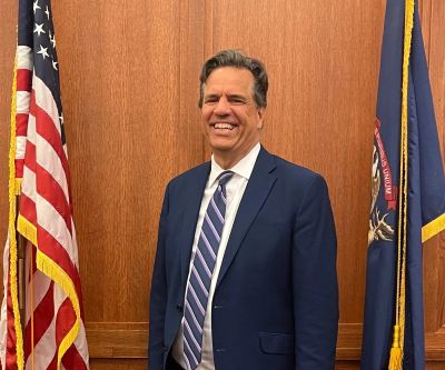 Man in suit smiling between two flags.