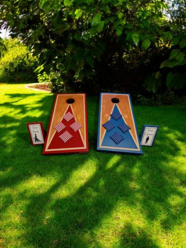 Two bean bag toss boards with red and blue bags set up on grass.