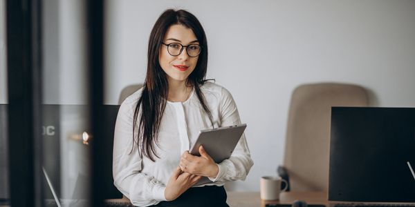 Woman in glasses holding a tablet in an office.