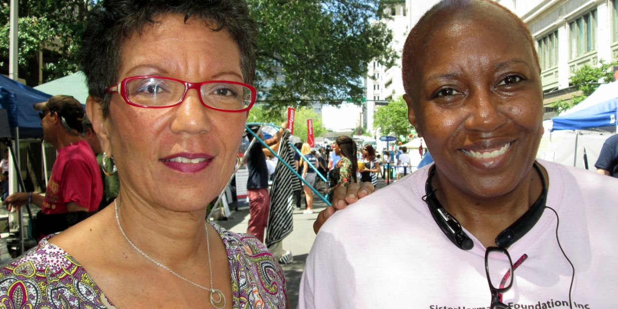Two women smiling outdoors at a sunny event.