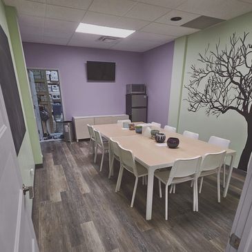 A modern conference room with a long table, white chairs, and a wall mural of a tree.