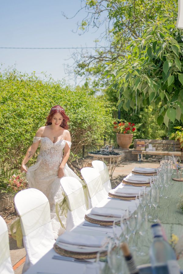 A bride in a lace wedding dress walks beside a beautifully set outdoor table.