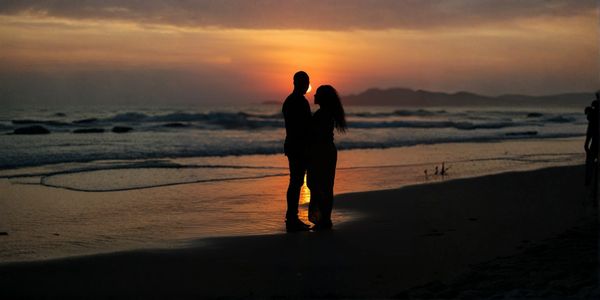Silhouetted couple embracing on the beach at sunset.