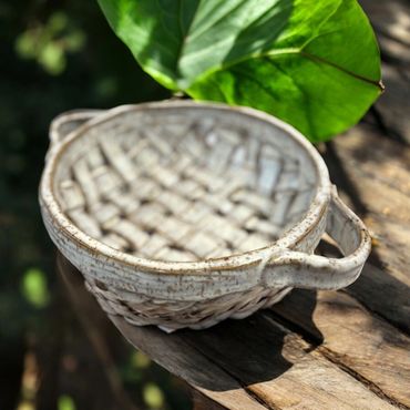 A ceramic basket-shaped dish with handles on a wooden surface.