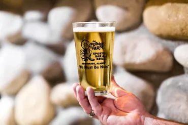 Peanut Farm branded beer glass held in front of stone wall