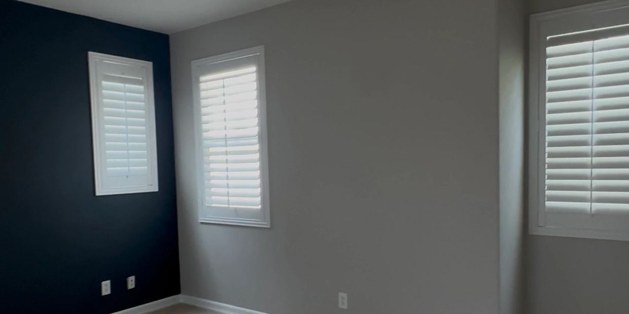 Empty room with dark and grey walls and three windows with blinds.