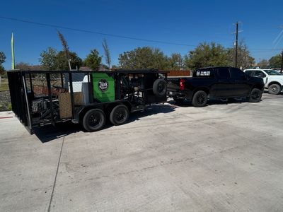 Black pickup truck towing a trailer full of junk and furniture on a sunny day.