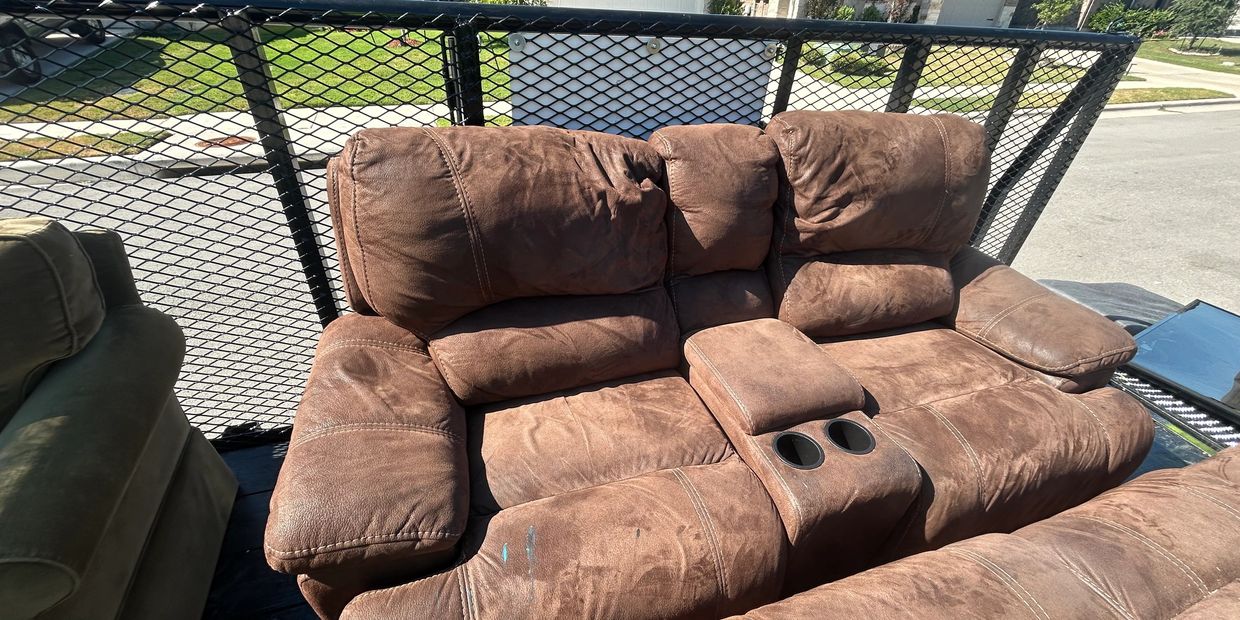 Brown reclining loveseat with cup holders on a trailer in a suburban neighborhood.