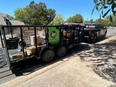 A black truck towing a trailer filled with junk removal items in a residential area.