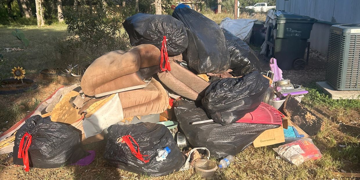 A pile of black garbage bags and old furniture outside a house.