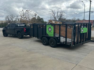Black truck with loaded trailer for junk removal service under a cloudy sky.
