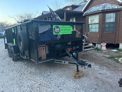 A junk removal trailer filled with items parked near a wooden house.
