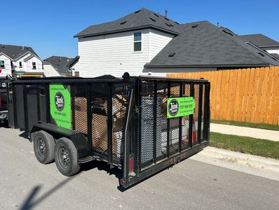 Black trailer filled with wood and debris parked on a suburban street.