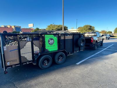 A black truck towing a trailer full of junk with a green Junk Squad sign.