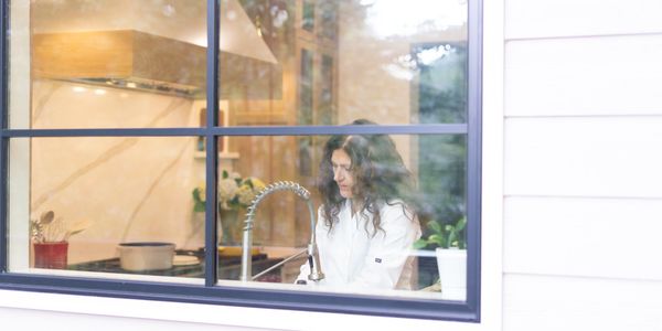 Woman washing dishes in a modern kitchen seen through a window.