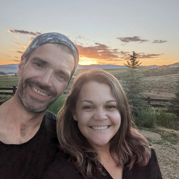 Smiling couple taking a selfie outdoors at sunset with scenic hills in the background.