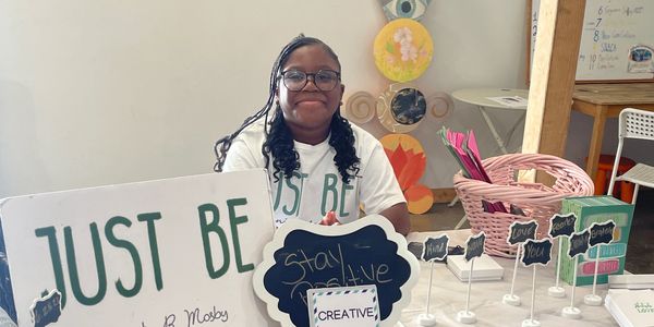 A woman sits behind a table with motivational signs and creative displays.