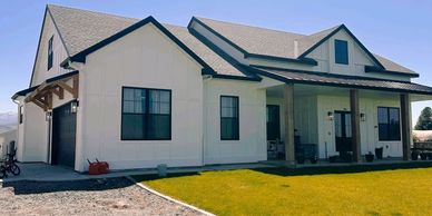Modern white farmhouse with black trim and spacious front porch under clear blue sky.