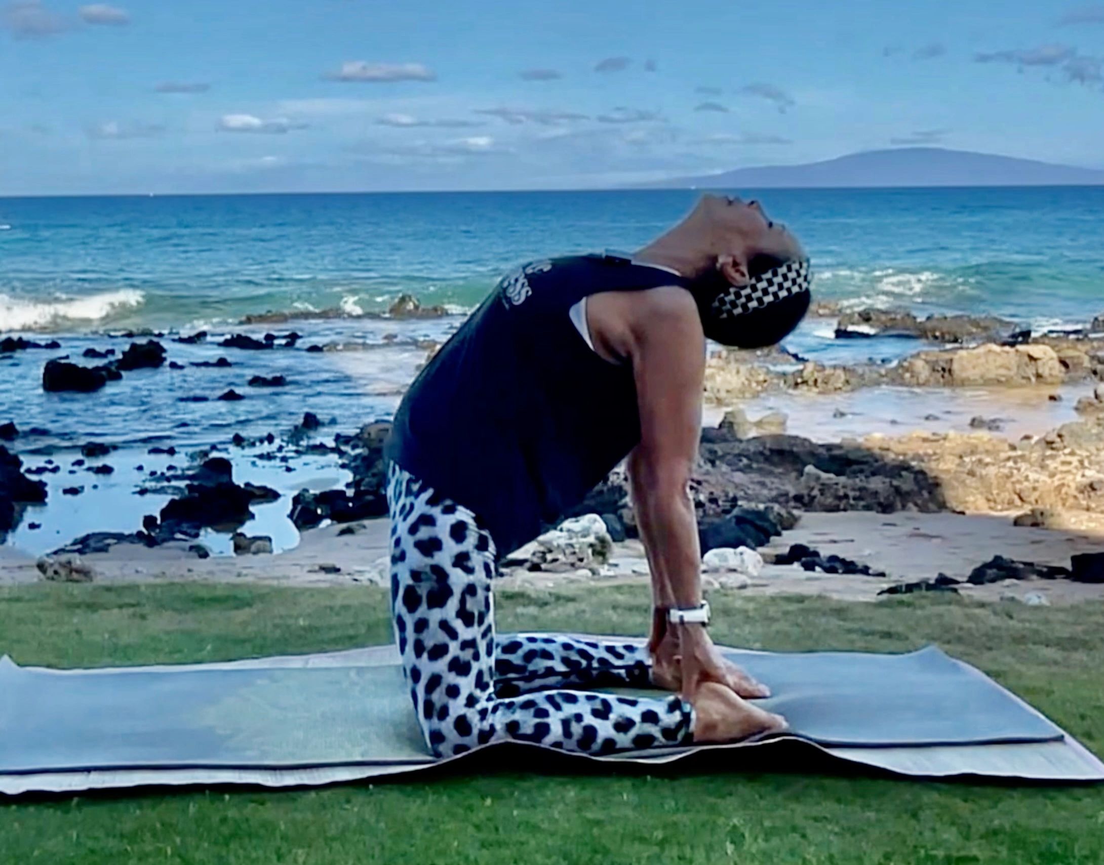 Person practicing yoga by the ocean, performing a backbend pose.