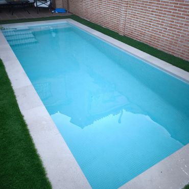 Piscina rectangular limpia junto a pared de ladrillo.