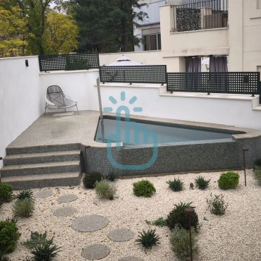 Piscina pequeña y jardín con piedras y plantas.