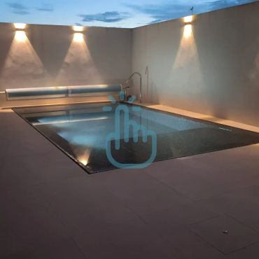 Piscina iluminada en un patio al atardecer.
