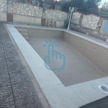 Piscina vacía en un patio con revestimiento de piedra.