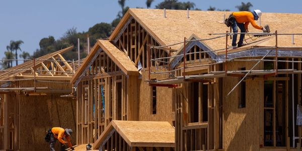 Construction workers framing wooden houses under clear sky.