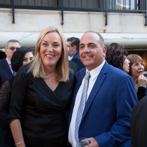 Two people dressed formally, smiling at an outdoor social event.