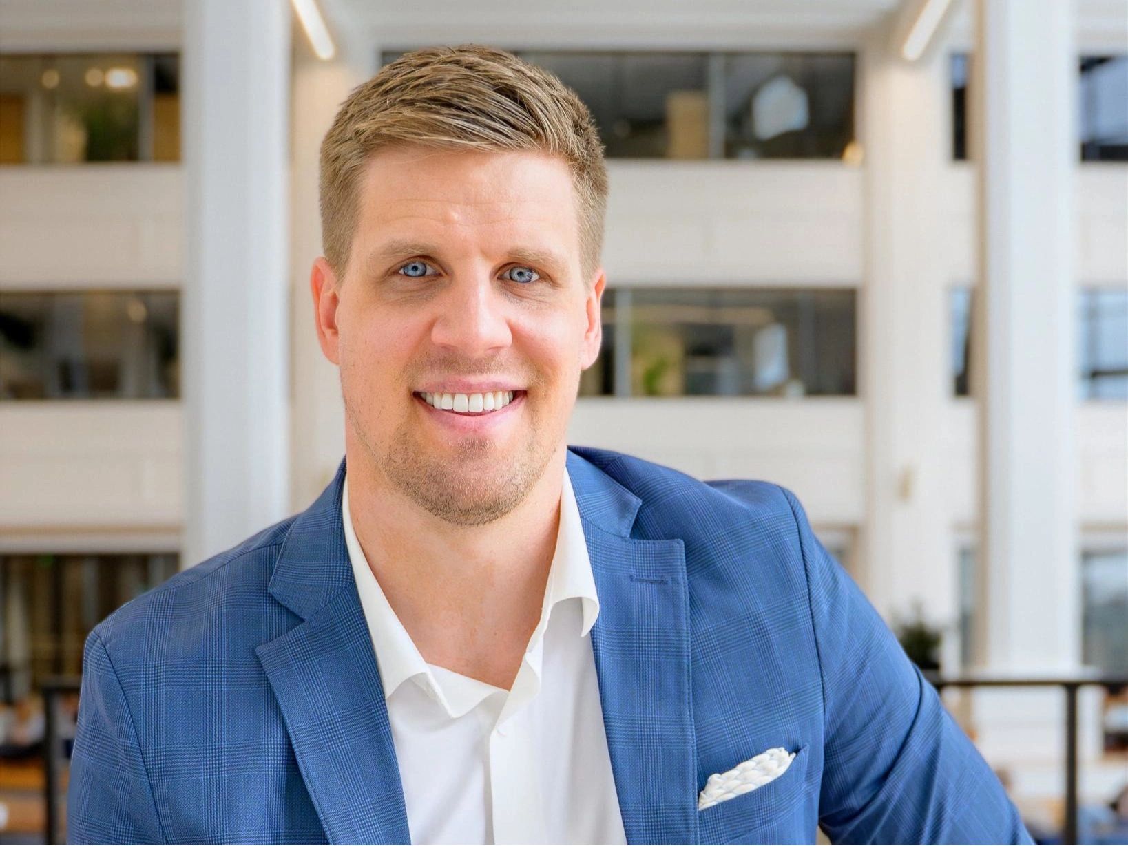 Smiling man in blue suit and white shirt in a modern office setting.