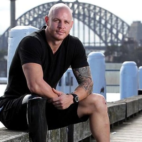Man sitting on a waterfront ledge with a bridge in the background.