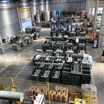 Industrial warehouse with electrical transformers and equipment organized in rows.