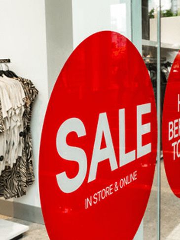 Red sale signs on a store window with clothes displayed inside.