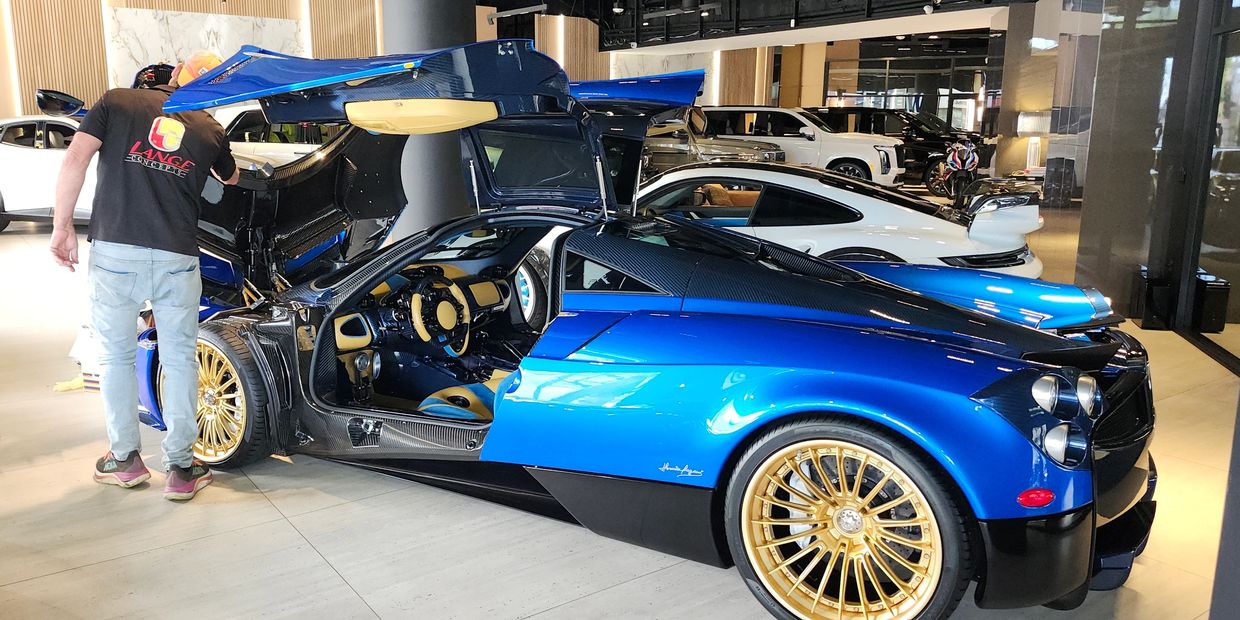 Blue sports car with butterfly doors and gold rims in showroom.