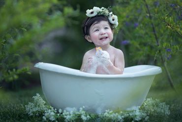 A joyful child in a flower crown enjoying a bubble bath outdoors.
