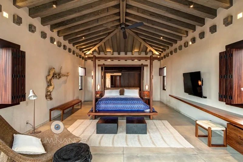 Dormitorio rústico con techo de madera, iluminación cálida indirecta y mobiliario de estilo tropical elegante.