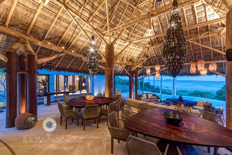 Palapa elegante con iluminación cálida, mesas de madera y vista al mar, ideal para reuniones