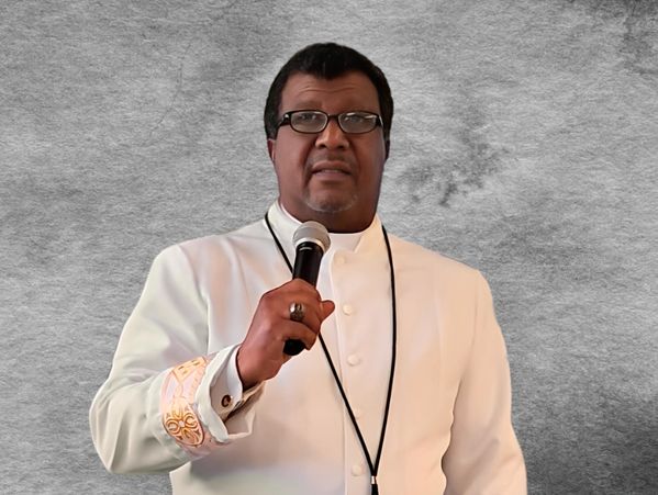 A man in white clerical attire holding a microphone.